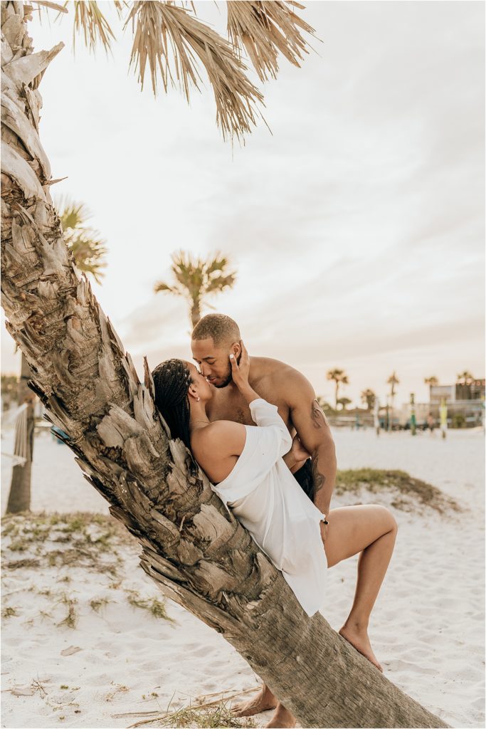 black couple on beach by palm tree engagement session