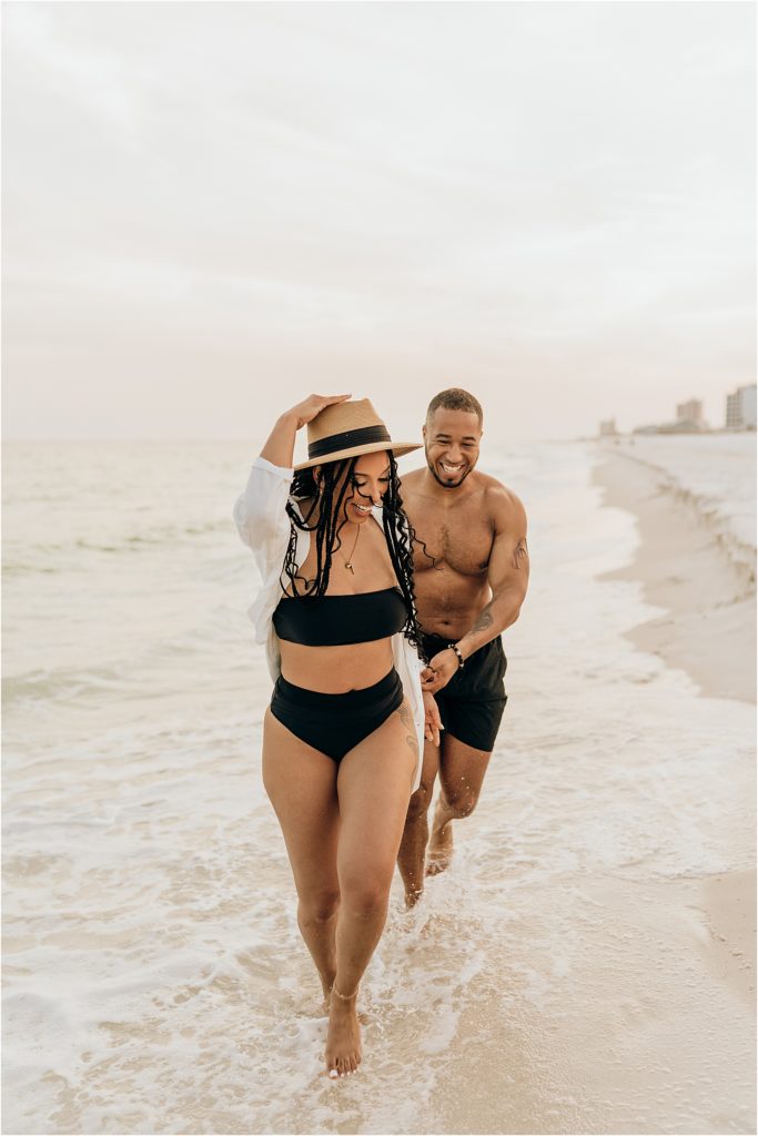 couple holding hands and running in swimwear on beach