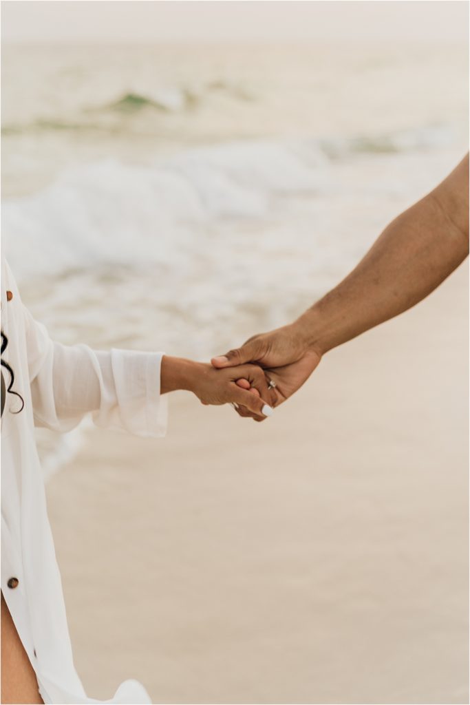 couple holding hands on beach showing engagement ring