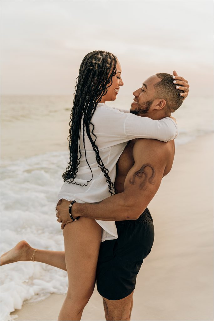 man lifting woman up on beach in swimwear