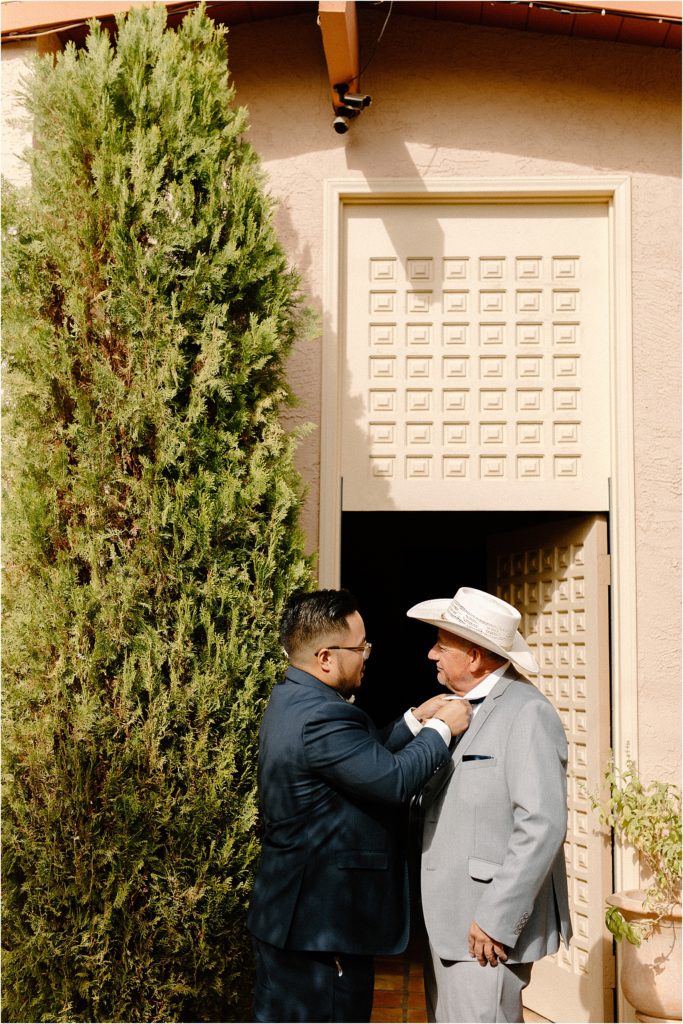 groom helping bride's dad with tie in front of childhood home at backyard palm springs wedding venue