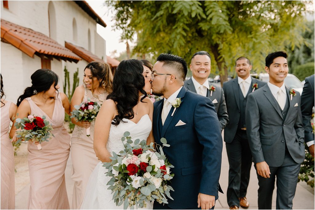 bride and groom kissing in front of wedding party at backyard palm springs wedding venue